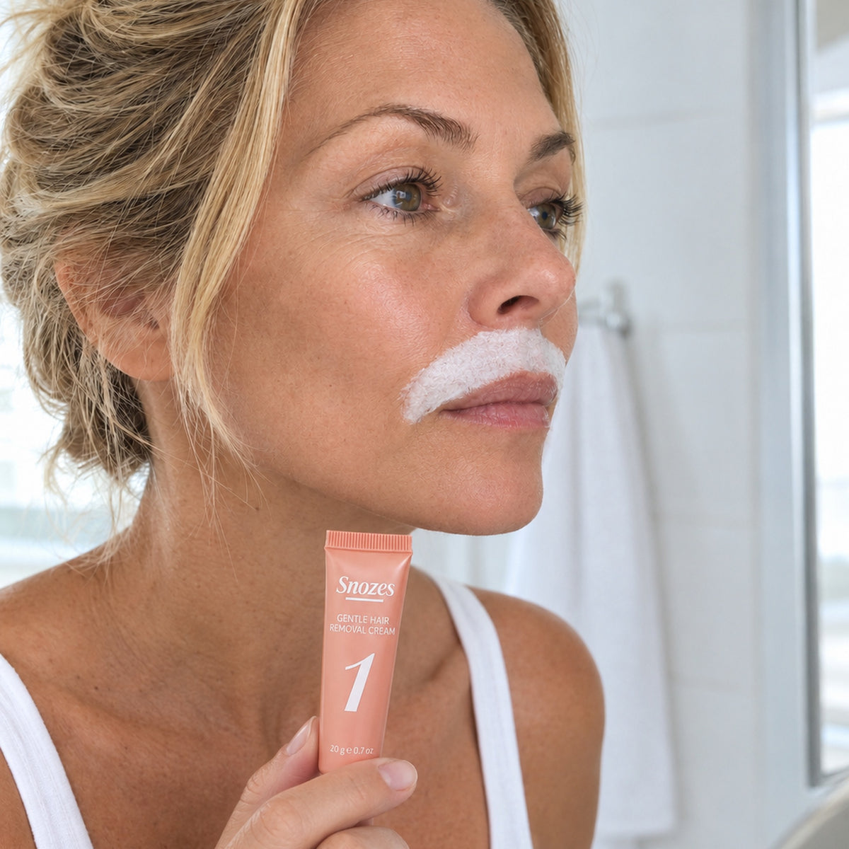 Woman with SNOZES hair removal cream applied on her upper lip, holding tube 1